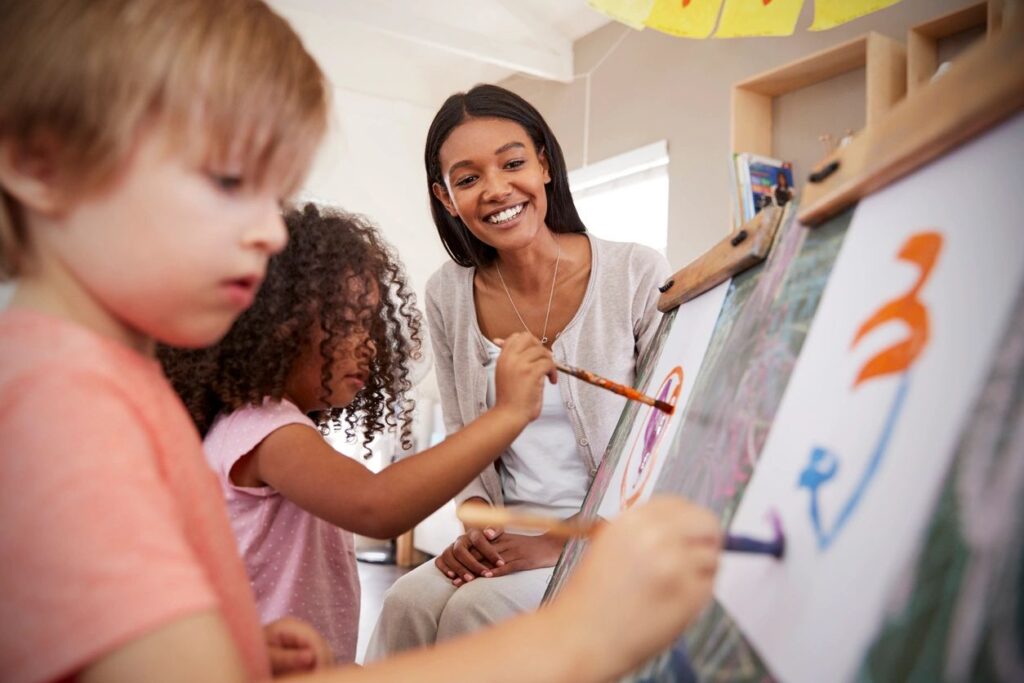 teacher smiling at children painting - employment opportunity