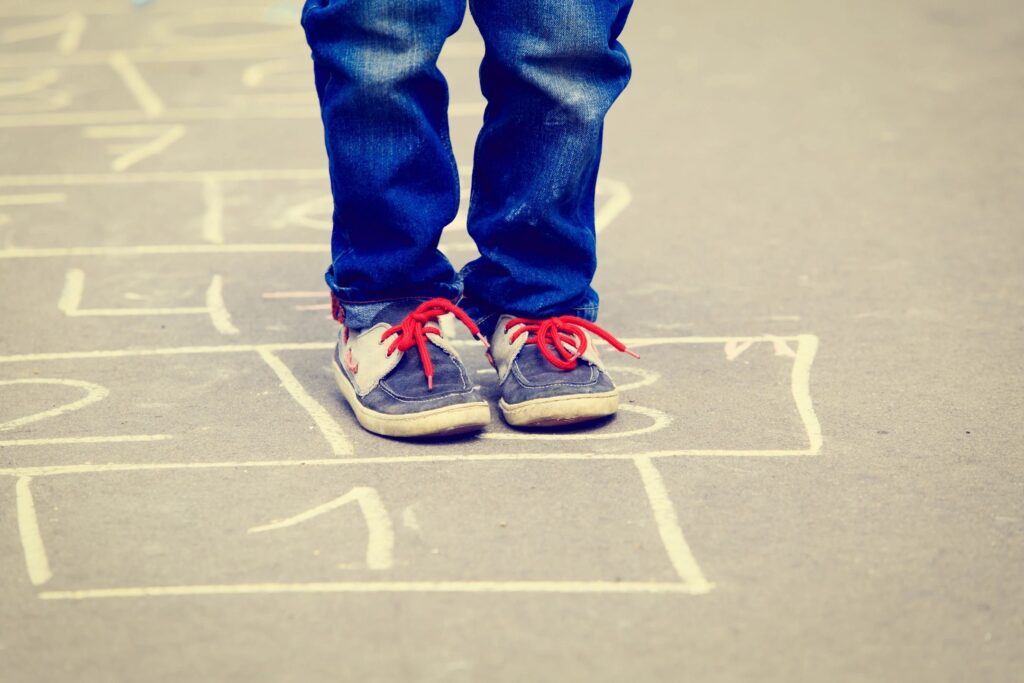 Child's feet in blue and white tennis shoes, side by side on hopscotch square.