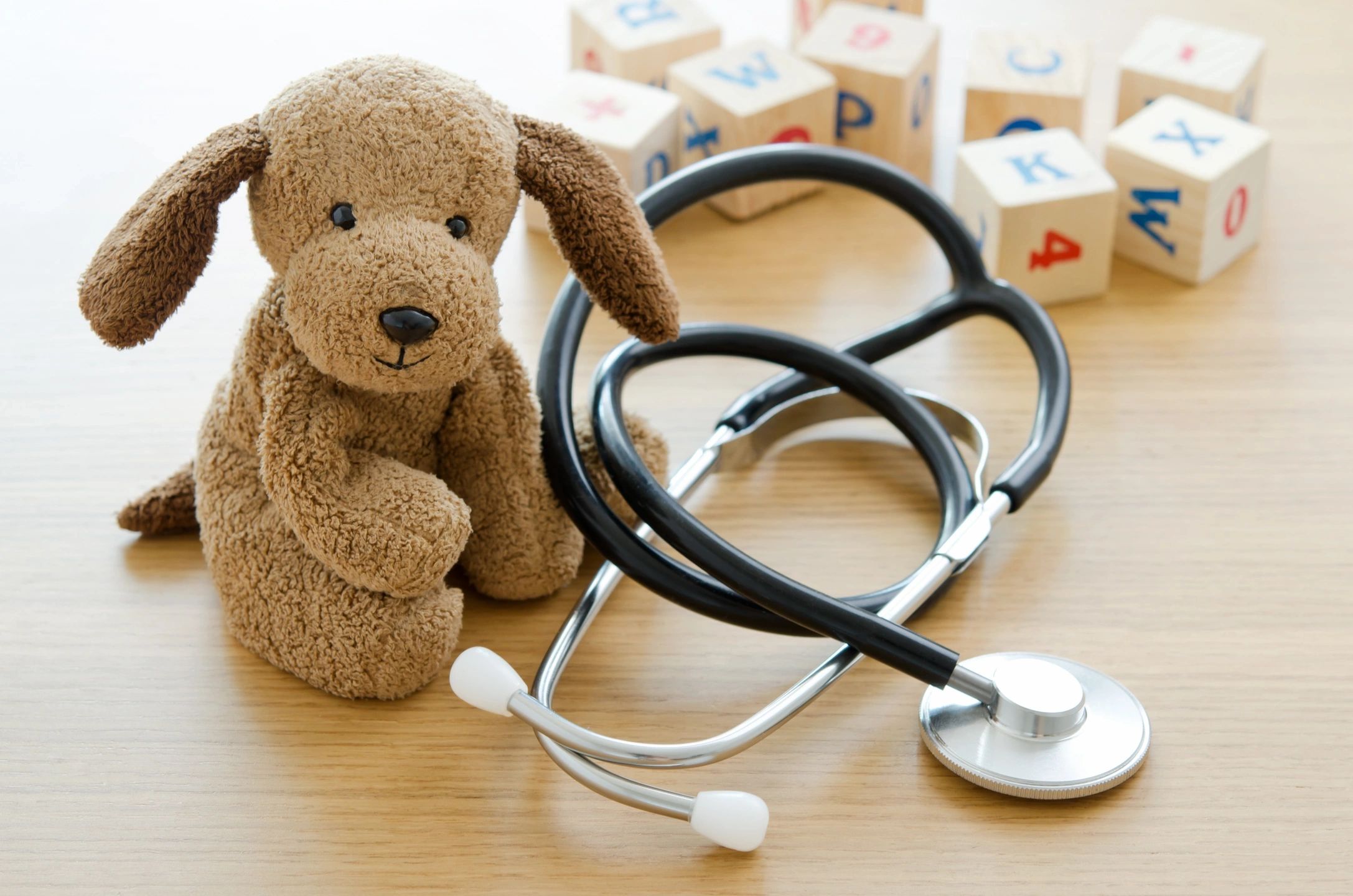 Stuffed brown dog and stethoscope on wooden table with children's building blocks behind.