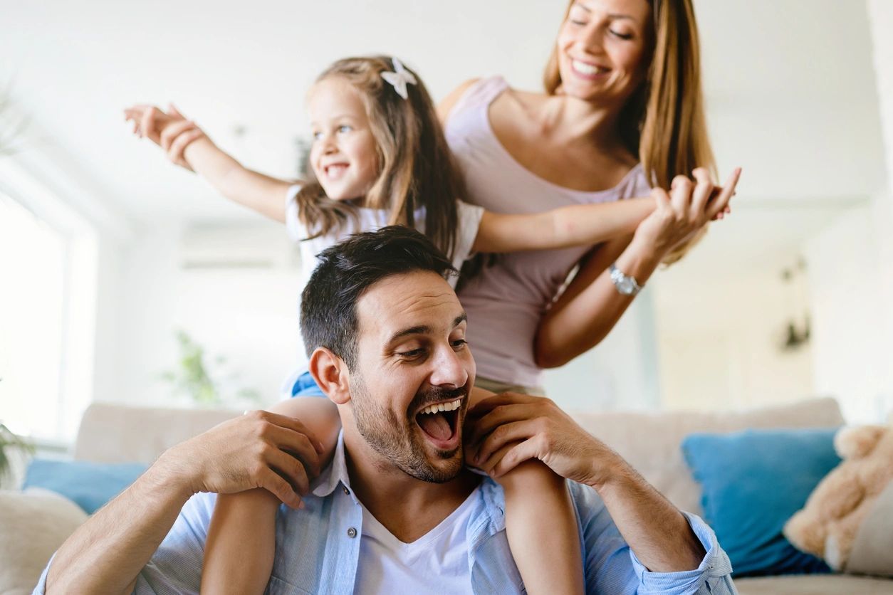 effective parenting creates a happy family like the one shown here. little girl sitting on her father's shoulders and mom supporting her from behind.